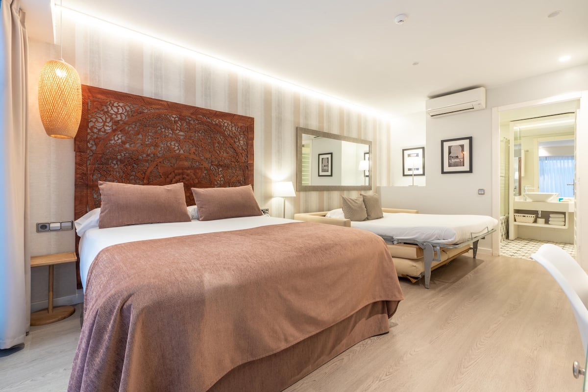 A hotel room with a large bed, a smaller bed, a mirror, and a bathroom visible through an open door.
