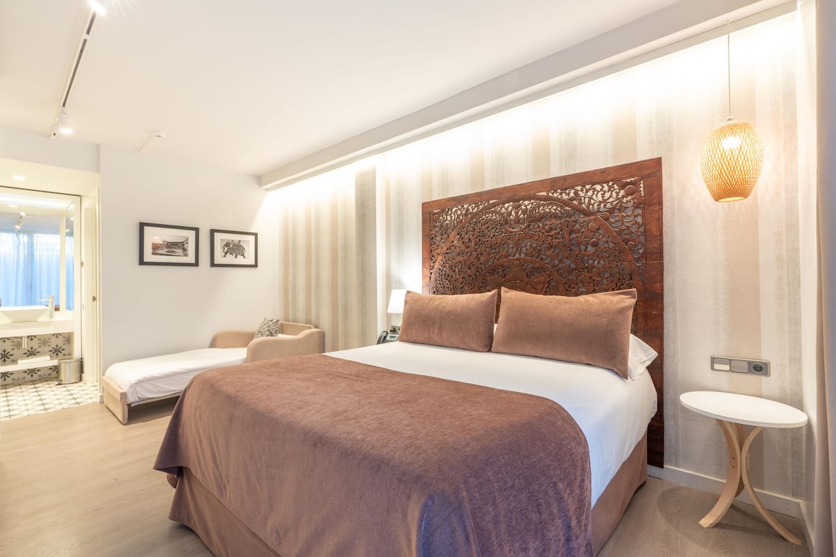 A modern hotel room with a large bed, a small bedside table, a chair, and a bathroom visible through an open door.