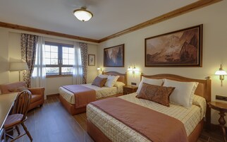 A hotel room with two beds, a chair, a lamp, and a painting on the wall.