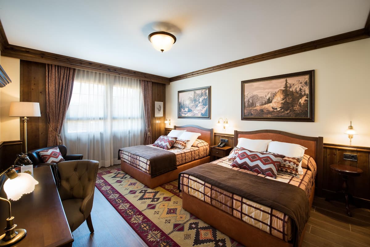 Une chambre d’hôtel avec deux lits, un bureau, une chaise et une lampe.