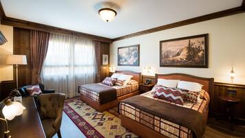 A hotel room with two beds, a desk, a chair, and a lamp.