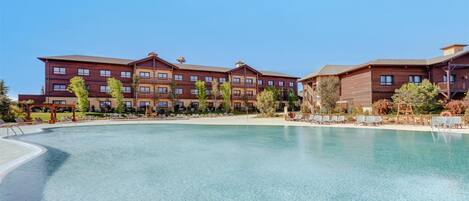 A hotel with a large pool, multiple floors, and a clear blue sky.