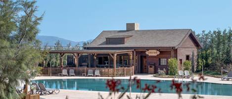 A lodge with a pool, outdoor seating, and a mountain backdrop.