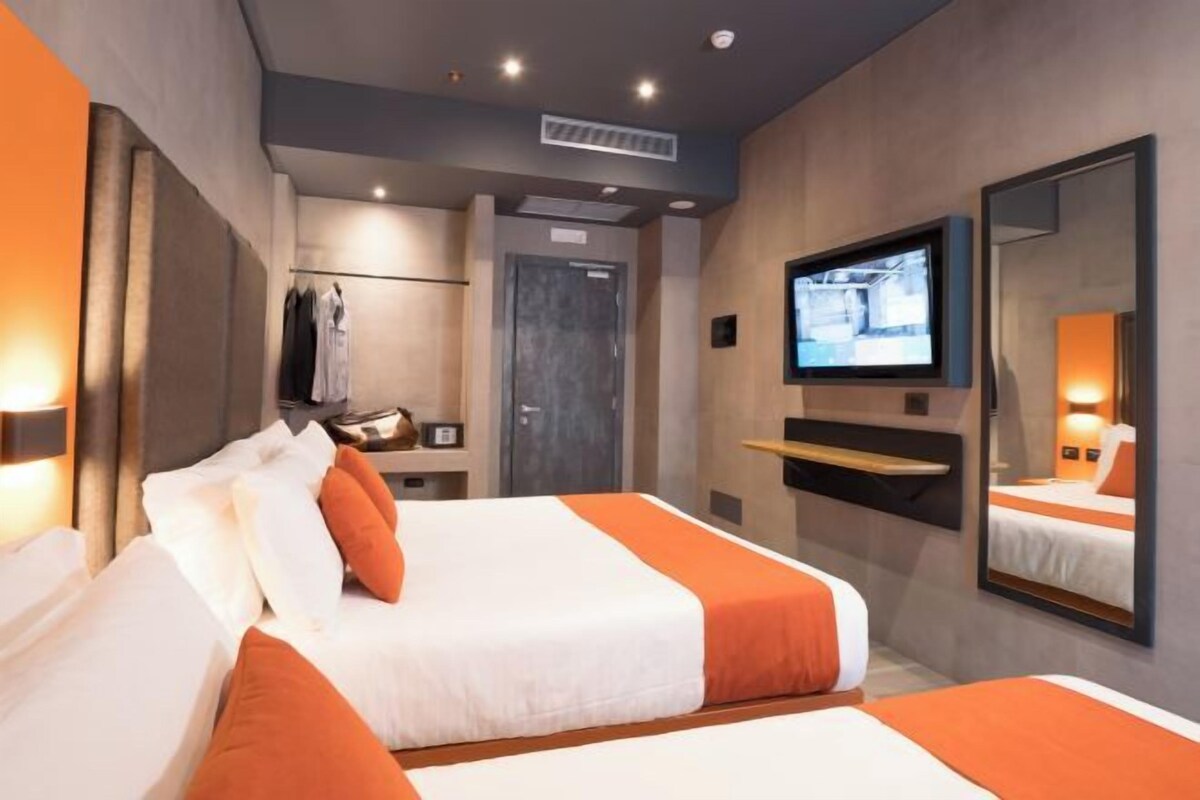 Una habitación de hotel moderna con dos camas, televisor, espejo y armario.