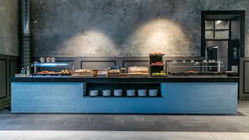 Disposição de buffet com diversos alimentos e acompanhamentos, balcão de tijolos azuis e parede de concreto com janela.