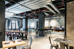 Un café moderne avec de hauts plafonds, des conduits apparents et un coin bar doté de tabourets et de chaises de bar.