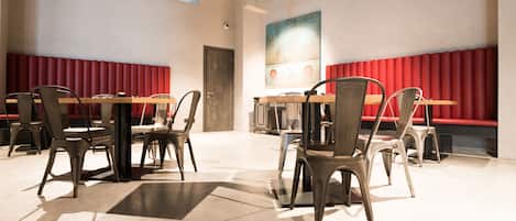 Un comedor moderno con mesas y sillas altas, asientos tipo banca con cojines rojos y un cuadro abstracto grande en la pared.