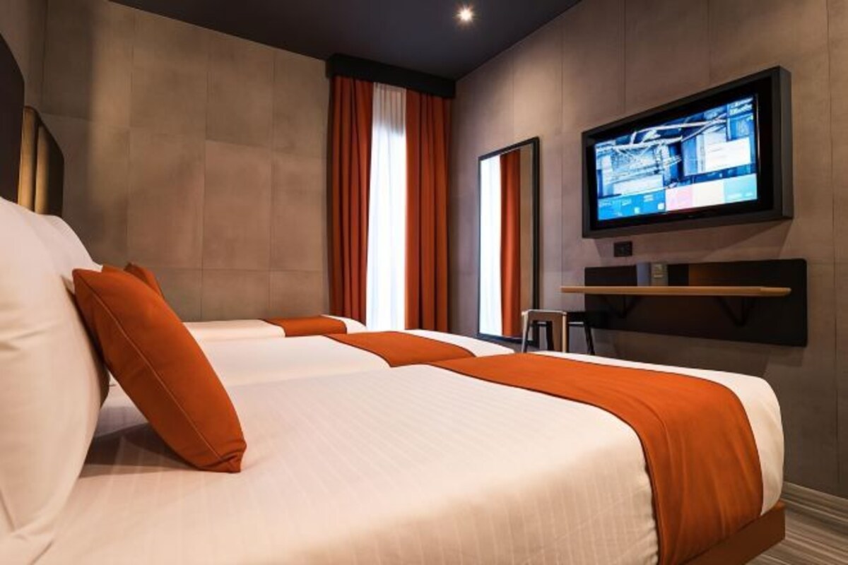 A hotel room with two beds, a television mounted on the wall, and a window with curtains.