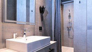 A modern bathroom with a large sink, a hairdryer mounted on the wall, and a shower area. - J24 Hotel Milano (Milan)