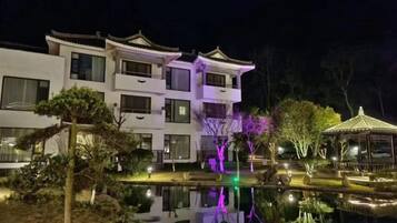 Un edificio de varios pisos con balcones, una fuente reflectante y un pabellón.