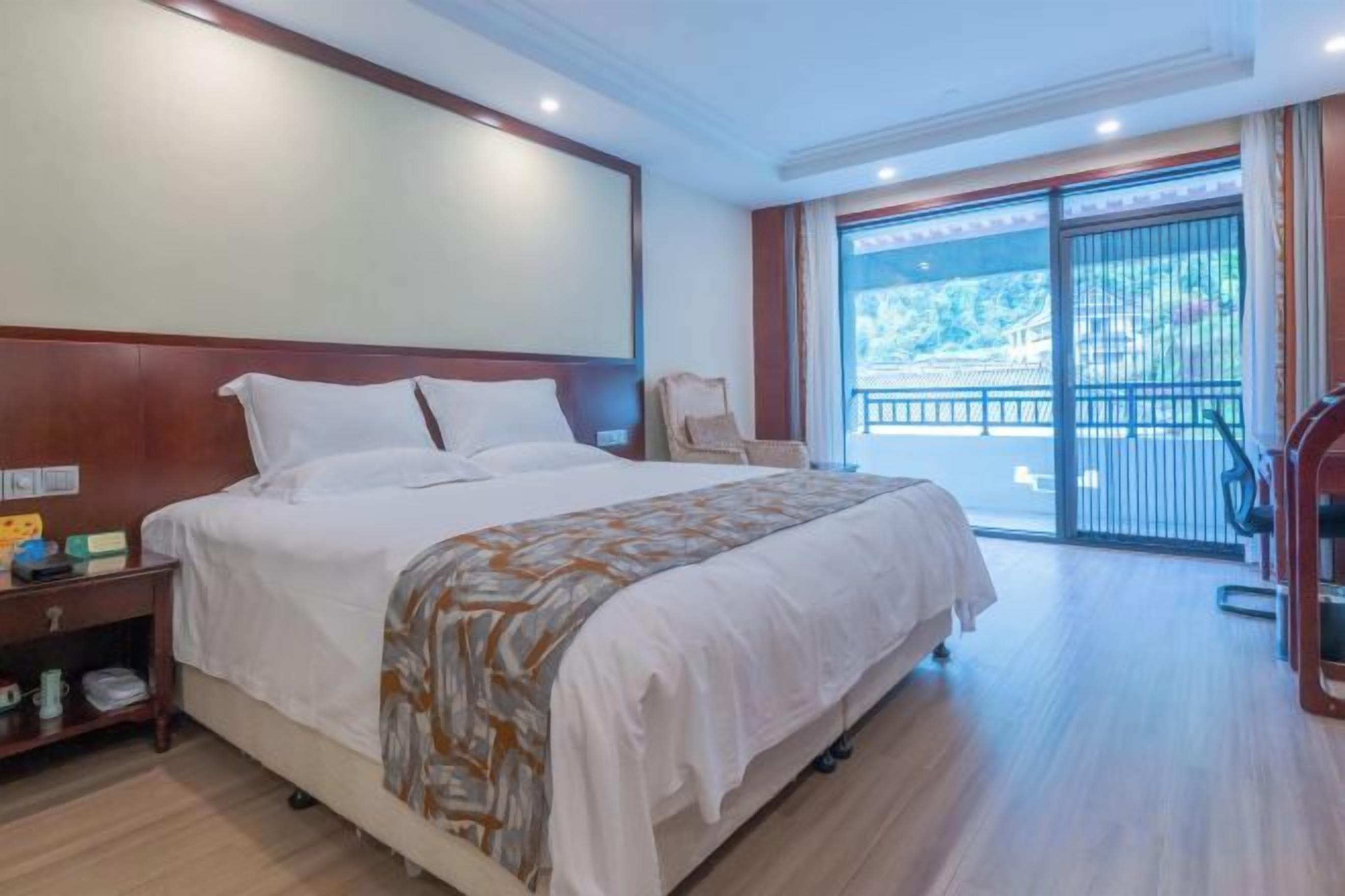 Habitación de hotel con una cama grande, una mesita de noche, una silla y vistas al exterior a través de una puerta corredera.