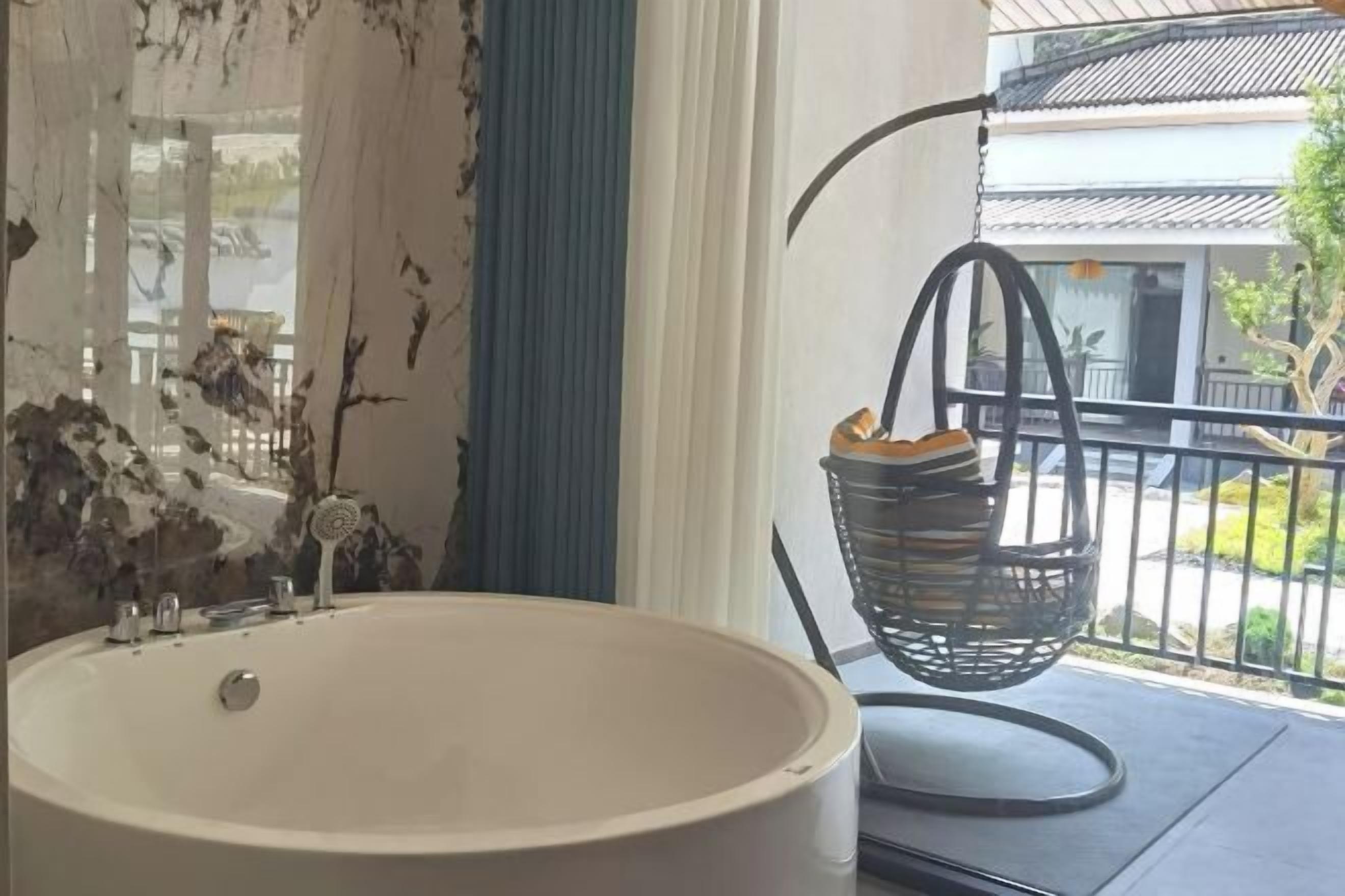 A bathroom with a large bathtub, a hanging basket with towels, and a view of a building outside.