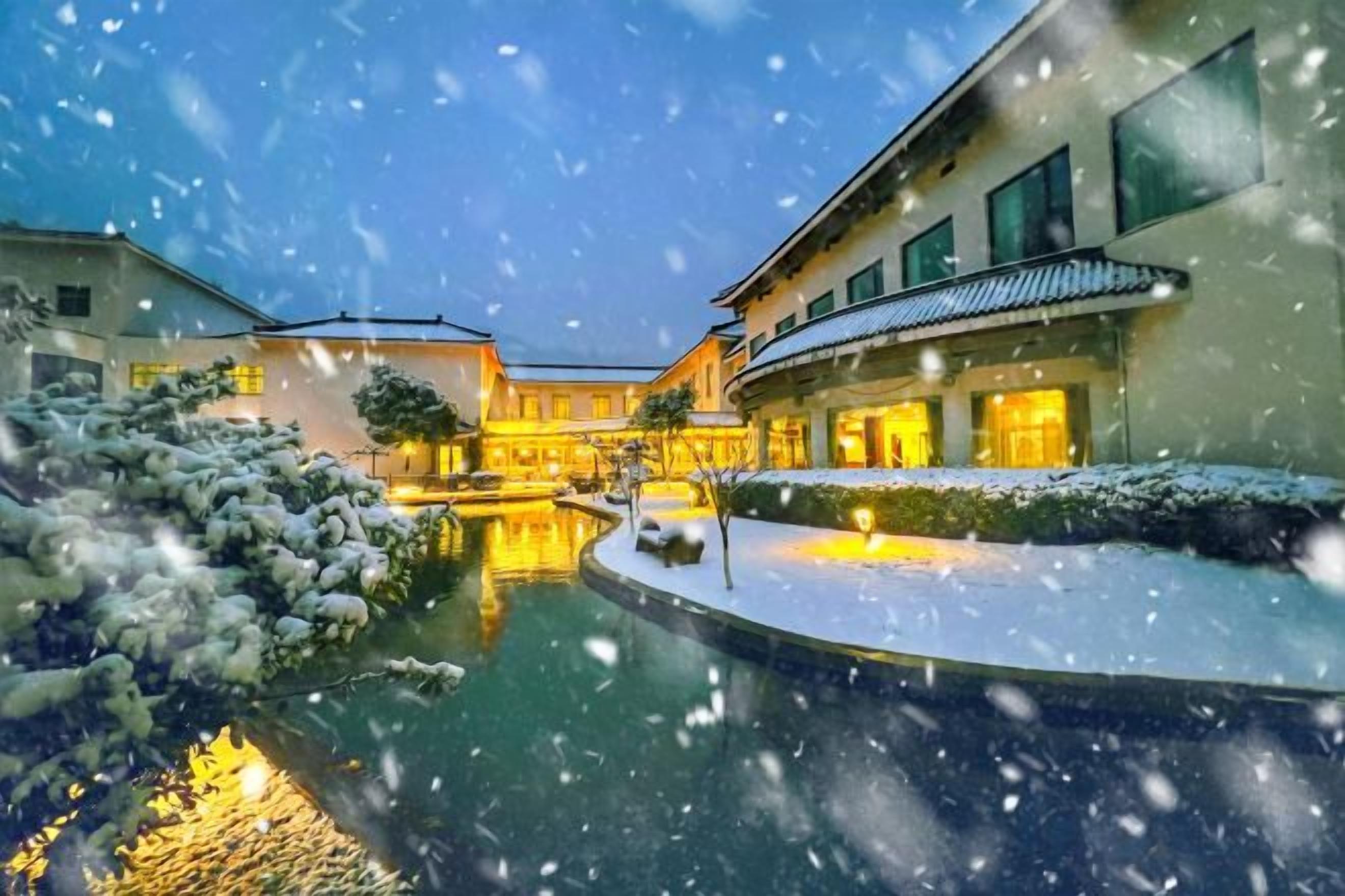 A courtyard with a pool, surrounded by buildings with warm lighting, and snow on the ground.