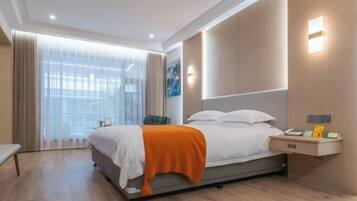 Una habitación de hotel moderna con una cama grande, una mesita de noche, un banco y vistas al exterior a través de cortinas translúcidas.