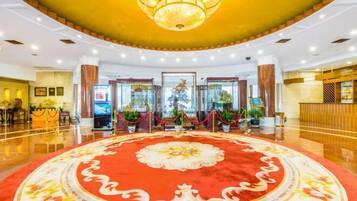 Un vestíbulo de hotel con una alfombra roja grande, un candelabro y una recepción.