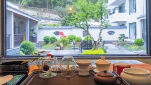 Et traditionelt japansk rum med tatamimåtter, et lavt bord med teudstyr og udsigt til en have gennem et stort vindue.