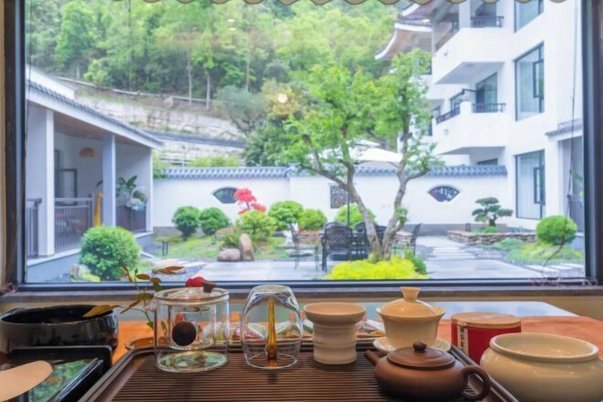 A traditional Japanese room with tatami flooring, a low table with tea utensils, and a view of a garden through a large window.