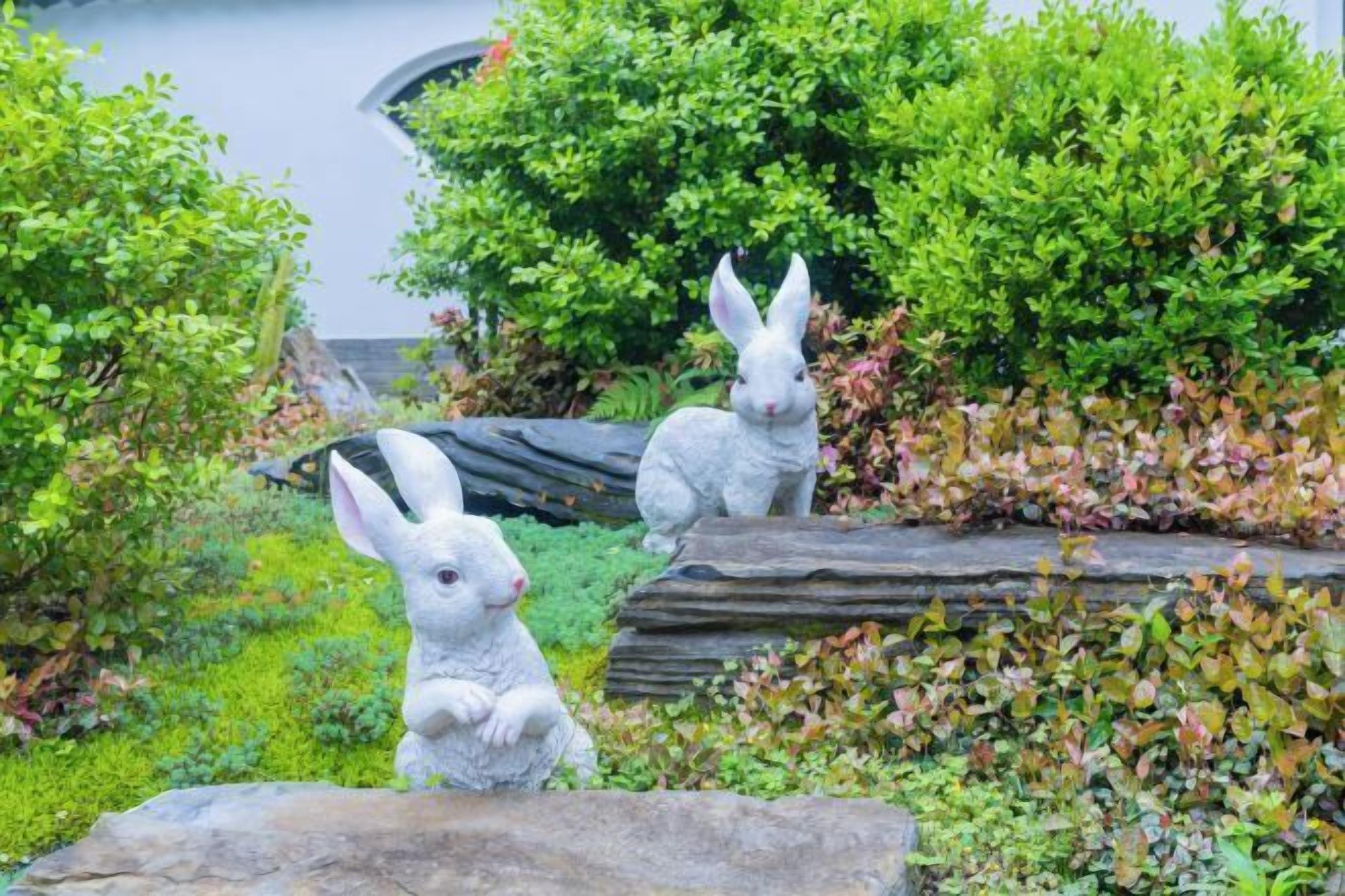 A garden with two white rabbit statues among green foliage and a wooden structure.