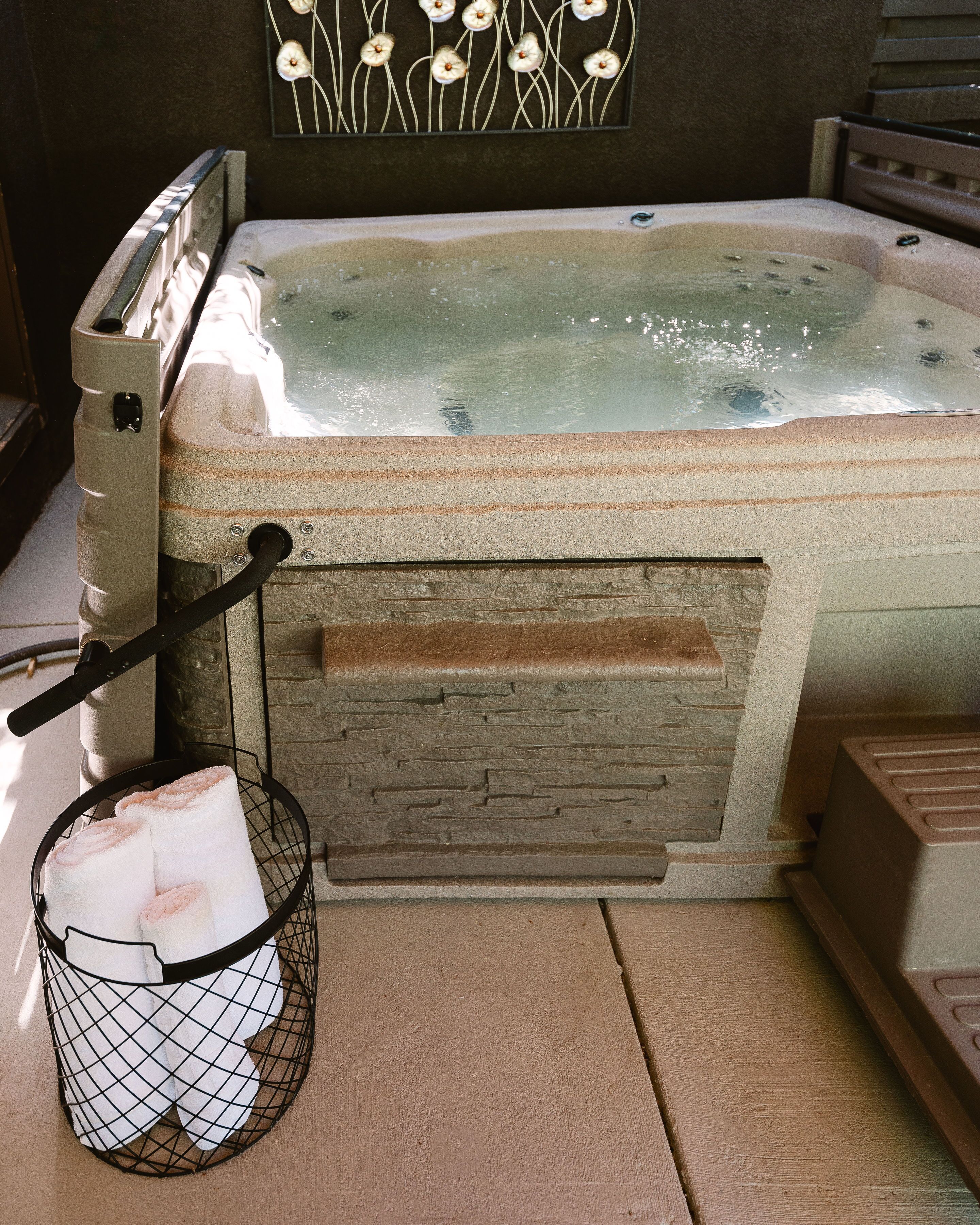 A hot tub with a stone exterior, a control panel, and a towel rack with towels.