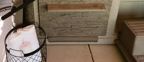 A hot tub with a stone exterior, a control panel, and a towel rack with towels.