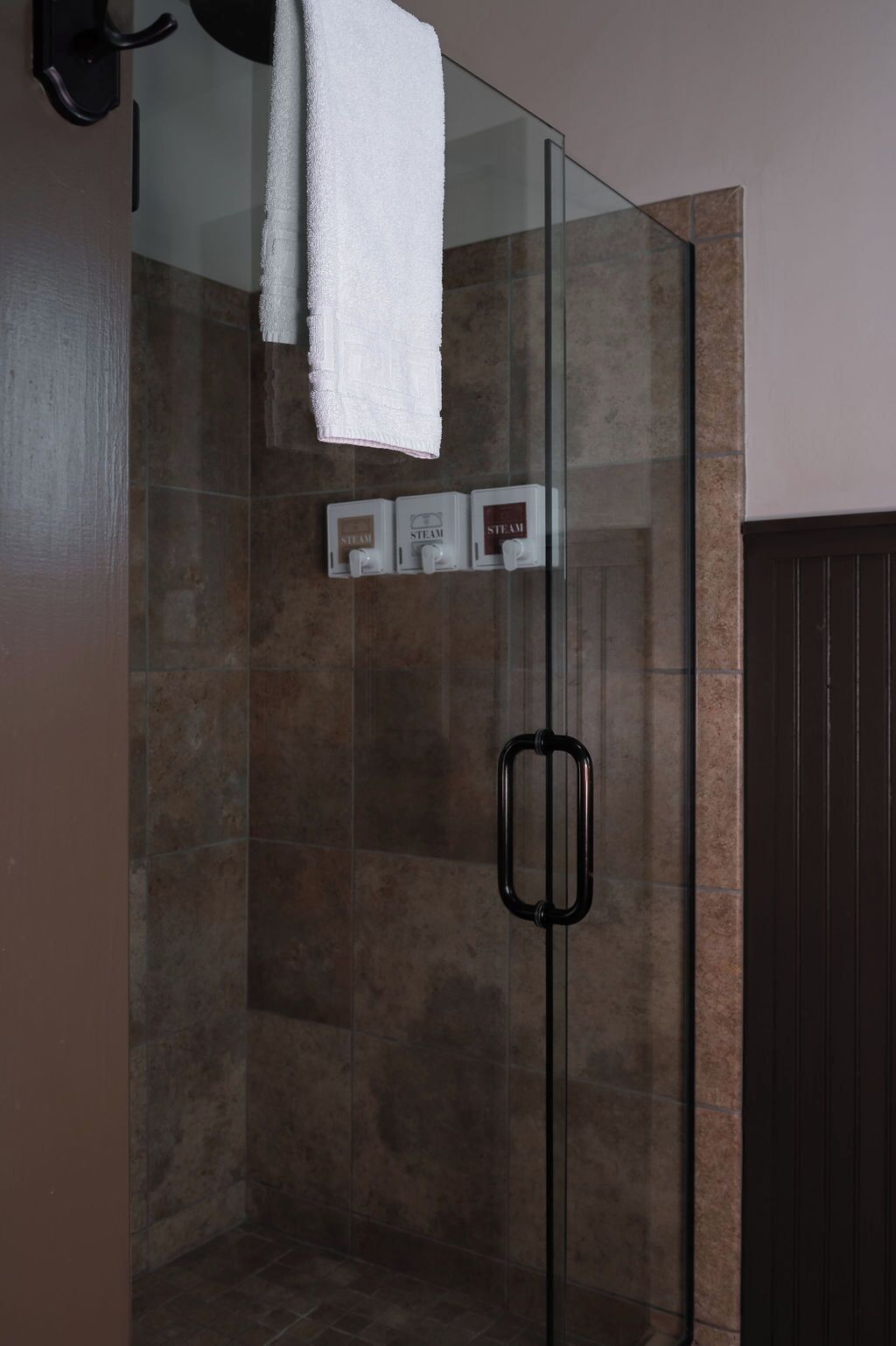 A glass-enclosed shower with a towel hanging on the wall, steam control buttons, and a black handle.
