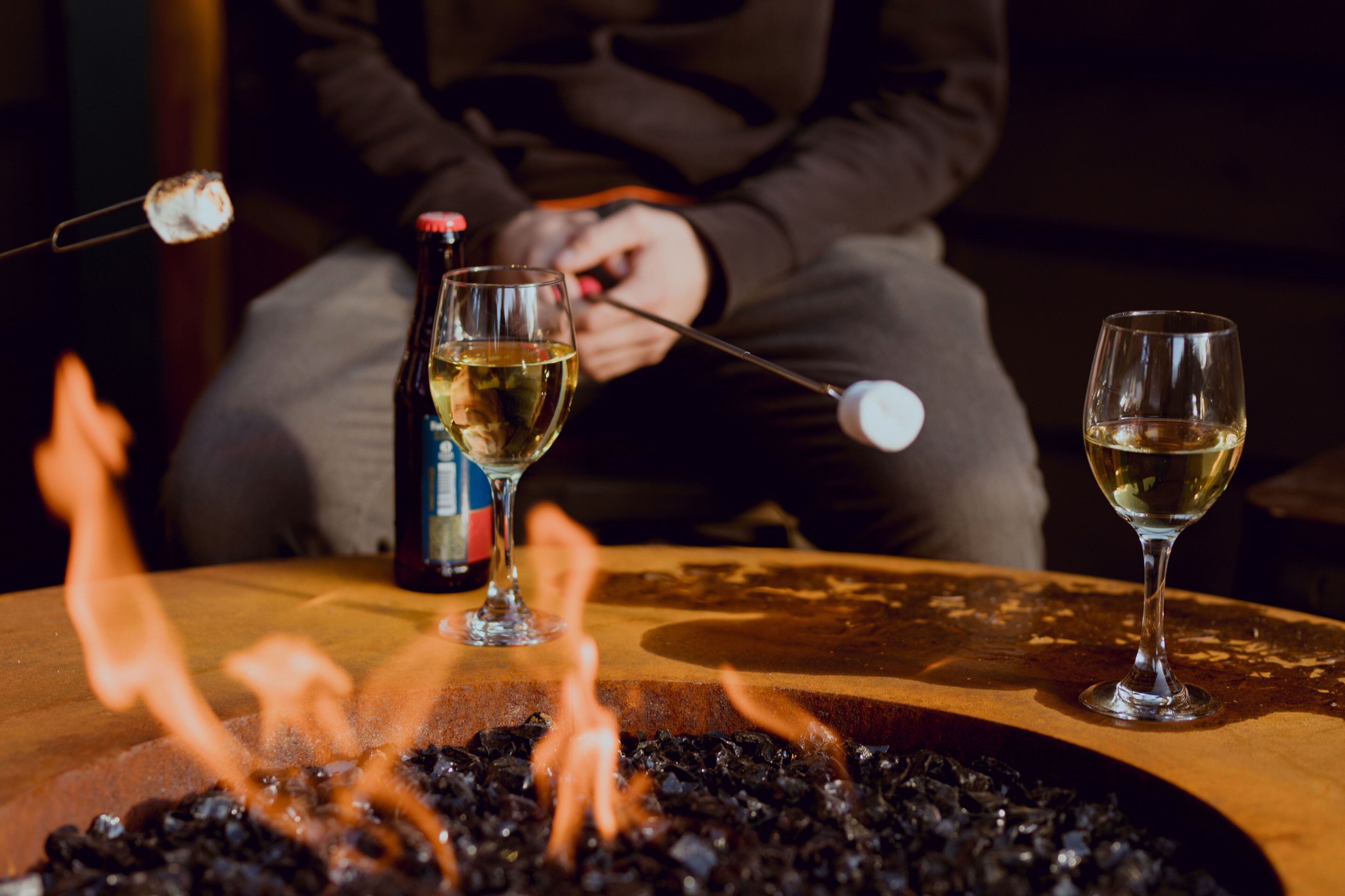A table with two glasses of white wine, a bottle of wine, and a fire pit with flames.