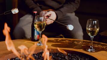A table with two glasses of white wine, a bottle of wine, and a fire pit with flames.