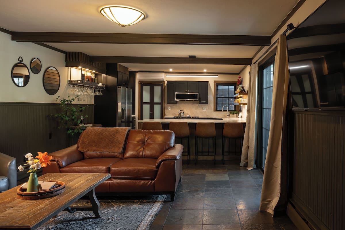 A modern living room with a leather sofa, a wooden coffee table, and a kitchen in the background.