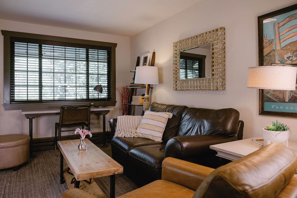 A cozy living room with a leather sofa, a wooden coffee table, and a window with blinds.