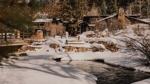 A snow-covered outdoor area with a stone bridge, wooden structures, and a river. - Highland Haven Creekside Inn (Evergreen)