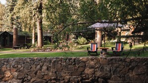 A stone wall with a picnic table and chairs, a small waterfall, and a gazebo in a wooded area. - Highland Haven Creekside Inn (Evergreen)