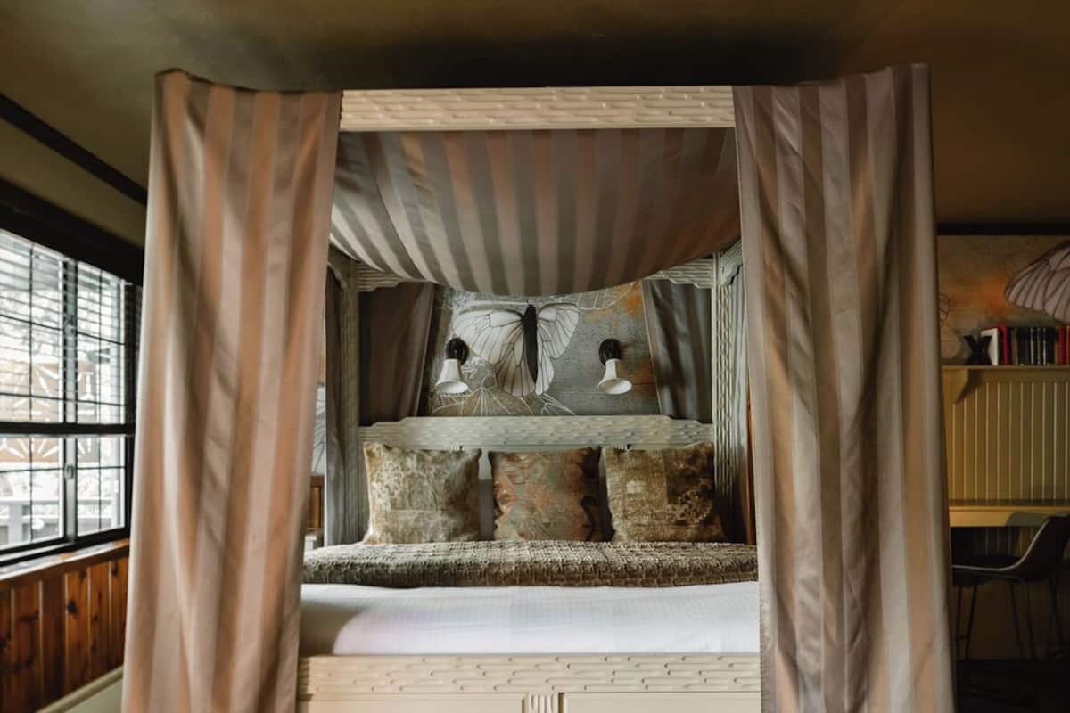 A four-poster canopy bed with a rustic design, featuring a wooden headboard and multiple pillows.
