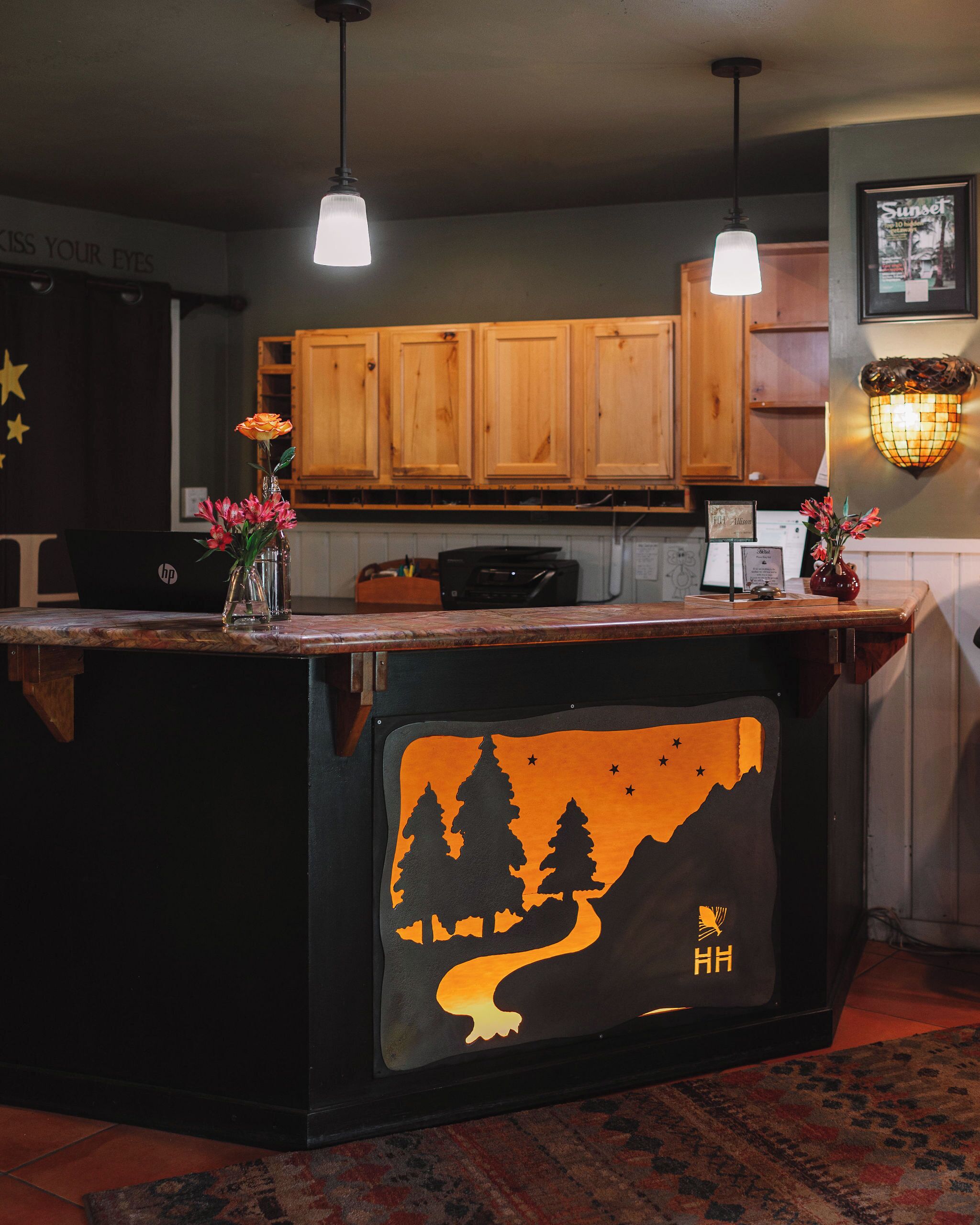 A kitchen with wooden cabinets, a black island with a mountain design, and a vase with flowers.