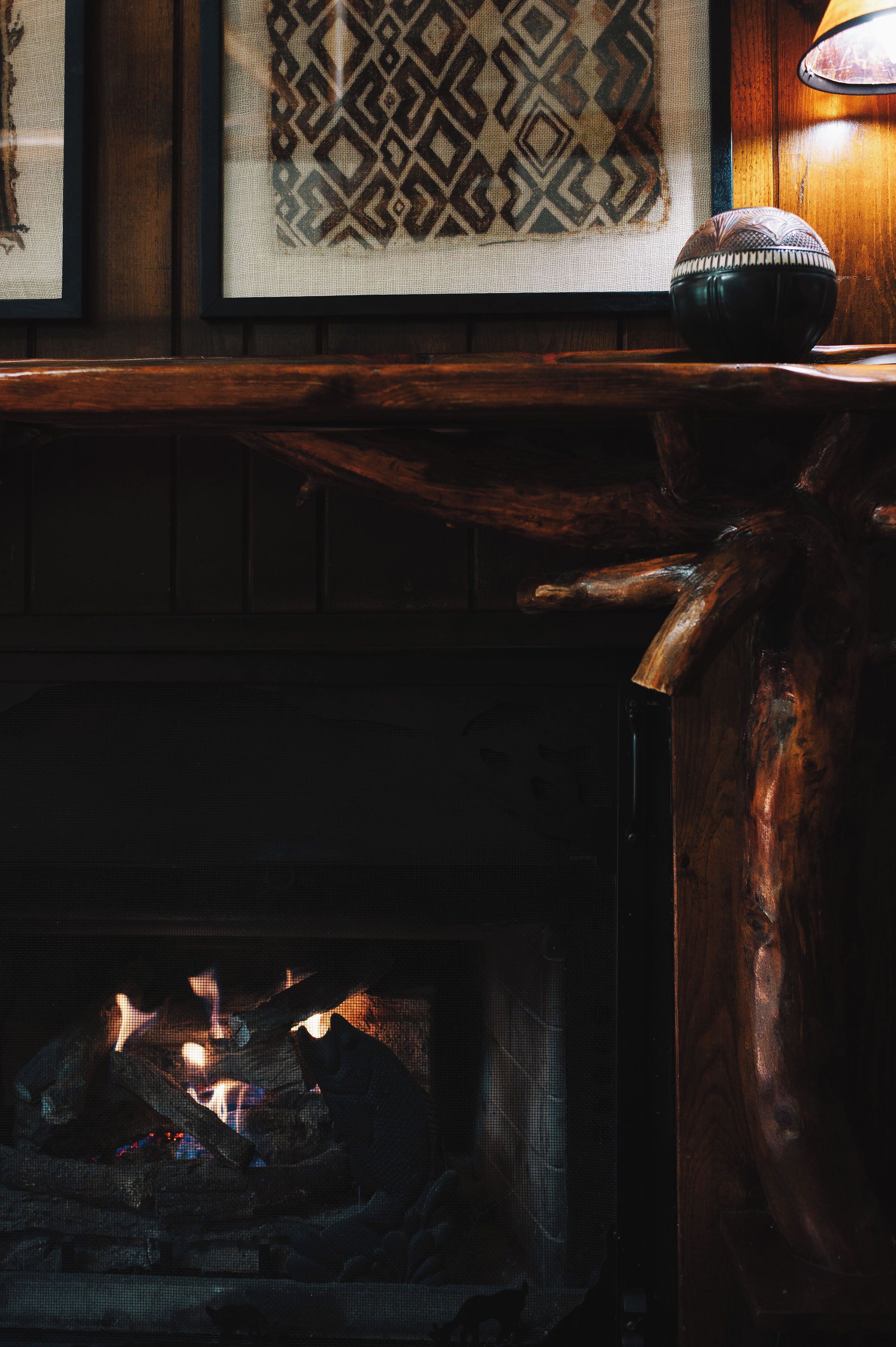 A fireplace with logs, a decorative bowl on the mantel, and framed artwork above.