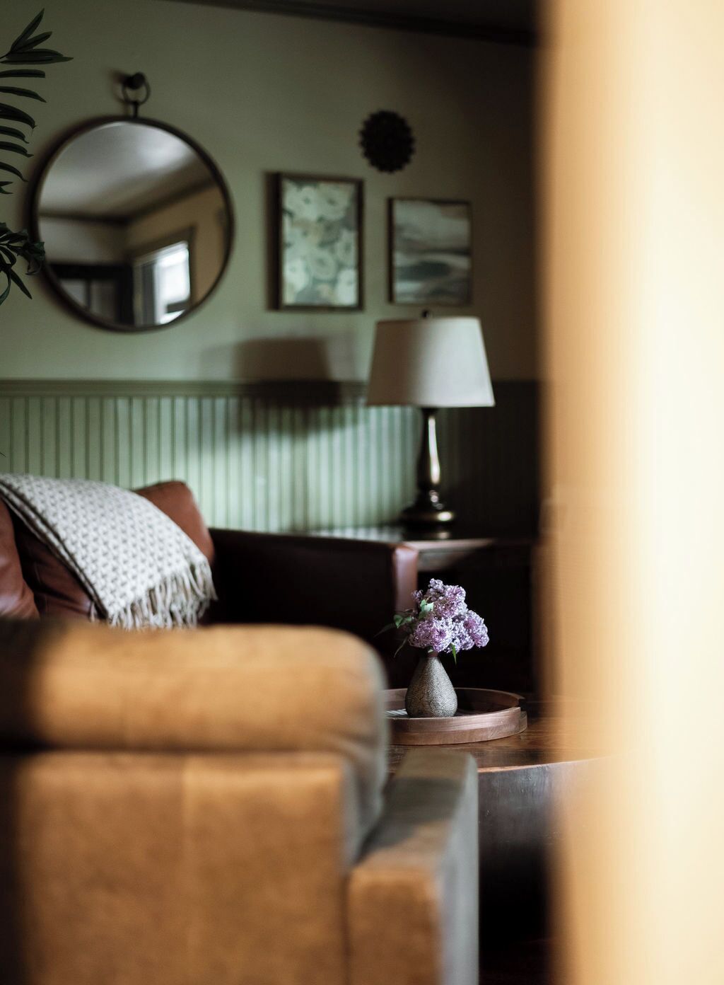 A cozy living room with a sofa, a lamp, and a vase with flowers.