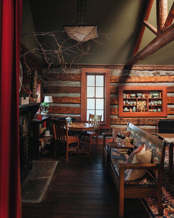 A rustic log cabin interior with a dining area, wooden furniture, and a display of pottery. - Highland Haven Creekside Inn (Evergreen)