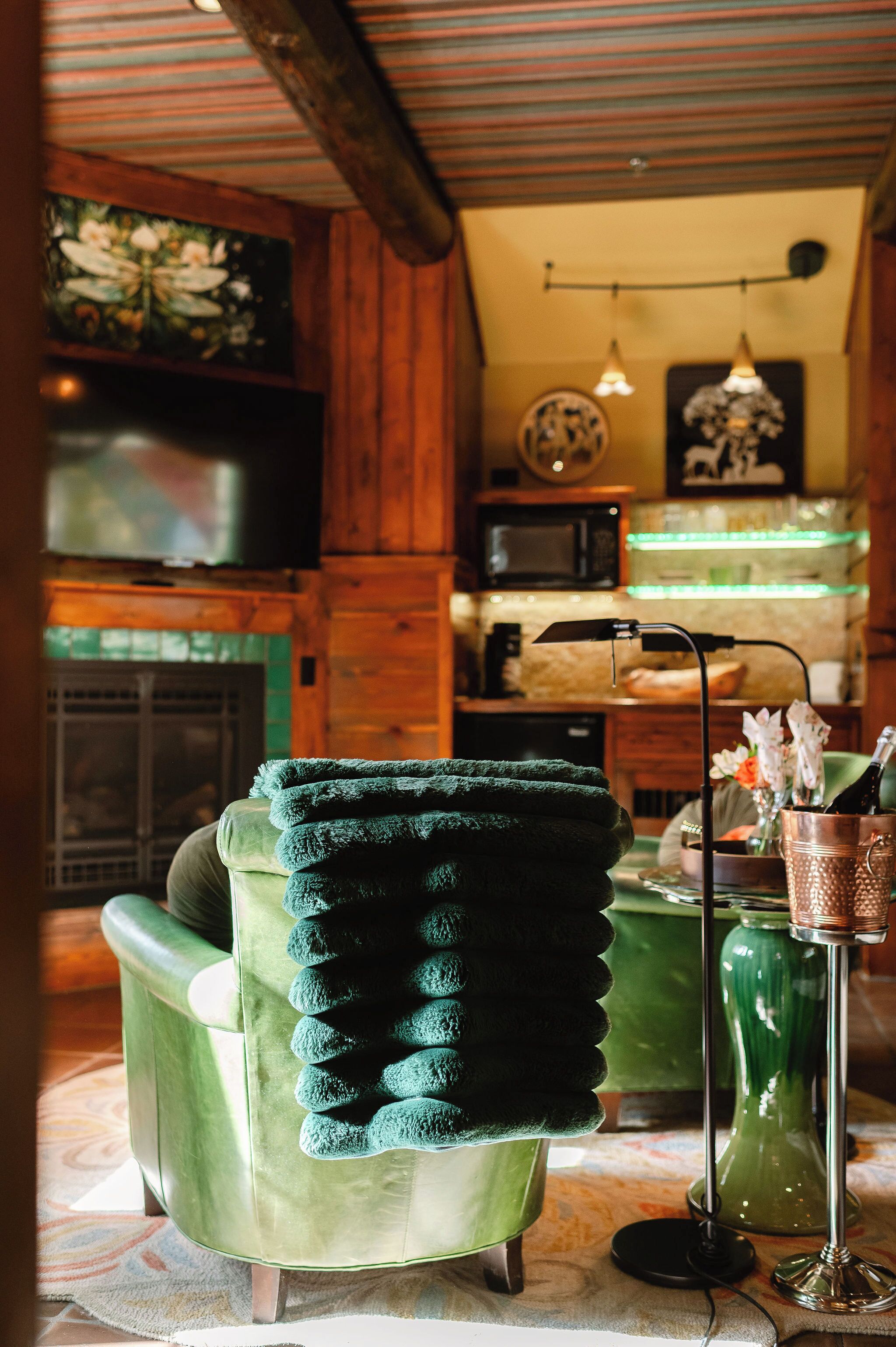 Une pièce chaleureuse avec un fauteuil vert, un téléviseur à écran plat, une cheminée et un vase vert rempli de fleurs.