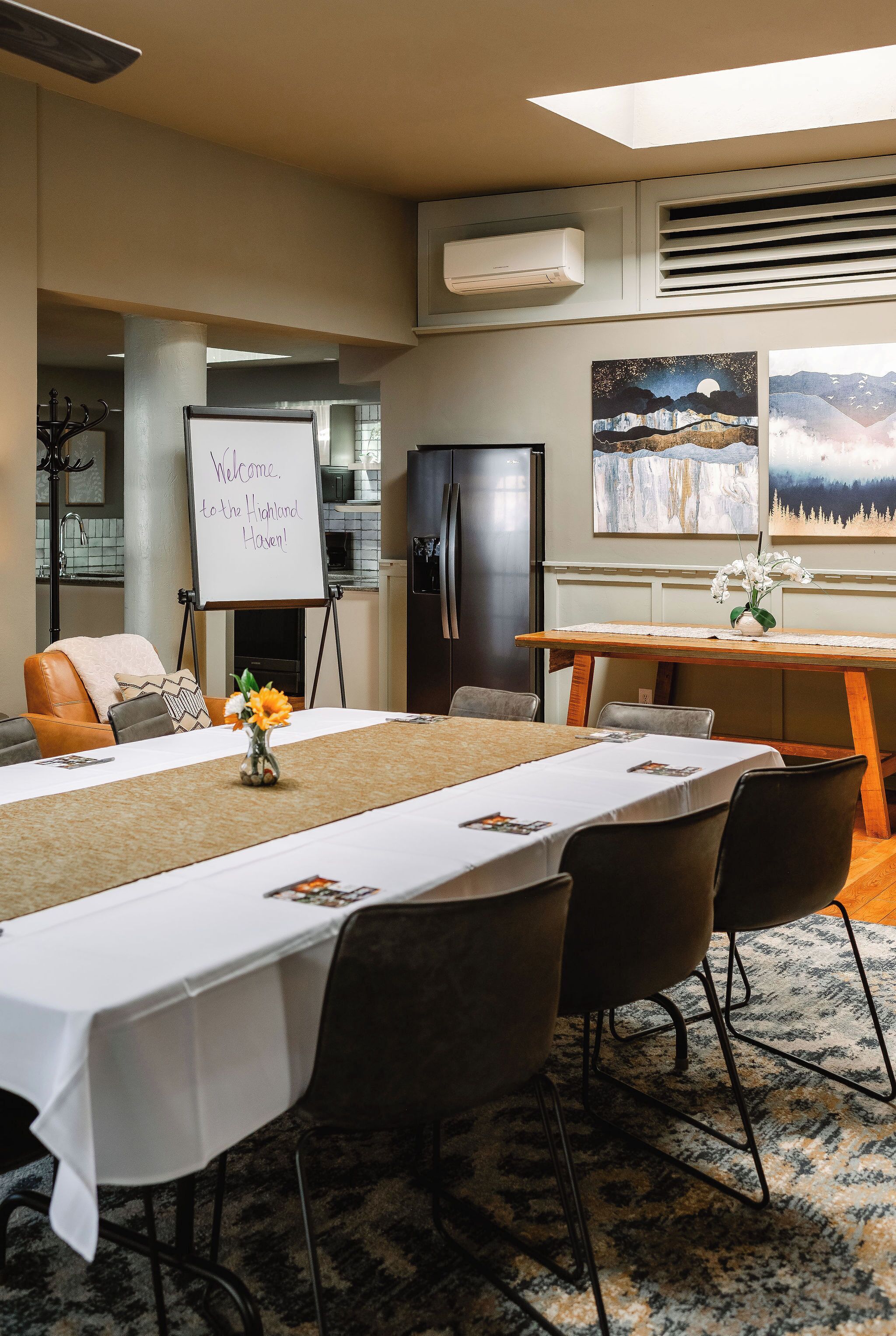 A conference room with a long table, chairs, a whiteboard, and artwork on the walls.