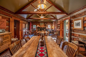 A rustic wooden dining room with a long table, chairs, and a decorative rug. - Highland Haven Creekside Inn (Evergreen)