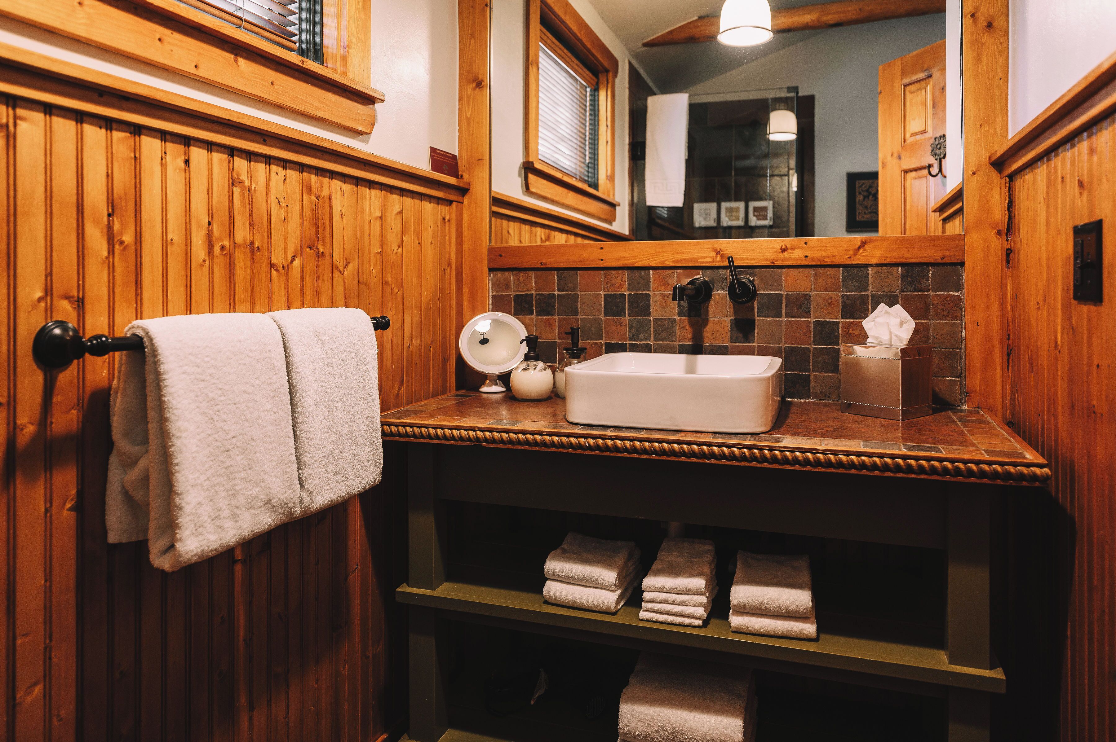 A wooden-paneled bathroom with a sink, mirror, and towel rack.