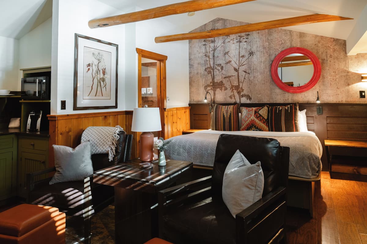 A cozy room with a bed, a wooden bench, a table with a lamp, and a framed picture on the wall.