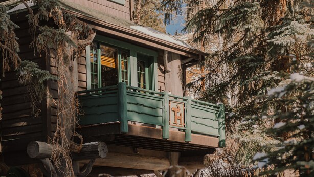 A wooden cabin with a balcony, surrounded by snow-covered trees. - Highland Haven Creekside Inn (Evergreen)