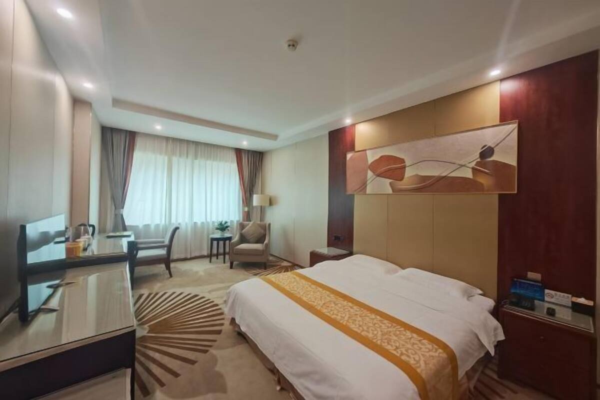 A hotel room with a bed, a desk, a chair, a lamp, and a painting on the wall.