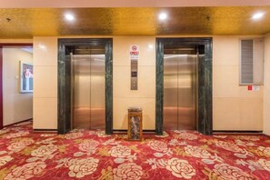 An elevator area with two elevators, a carpeted floor, and a wall-mounted sign. - Guangyun Hotel Beijing (Beijing)