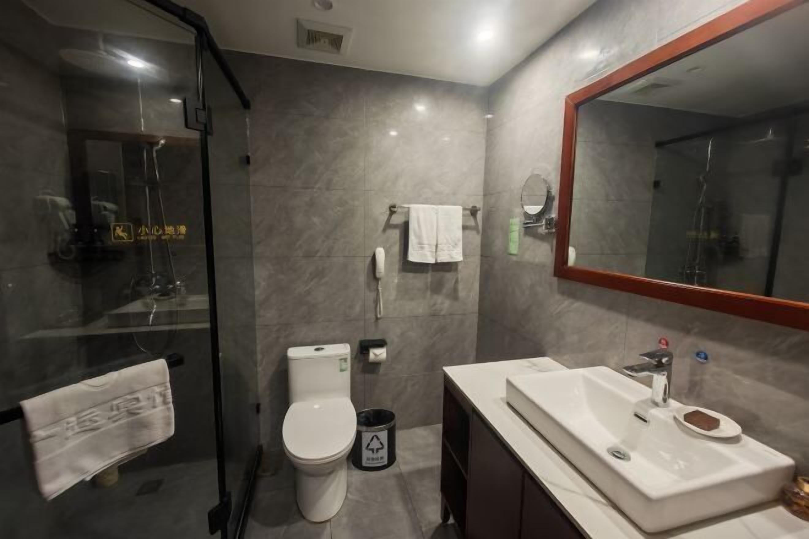 A modern bathroom with a glass shower enclosure, a toilet, a sink with a mirror, and a trash bin.