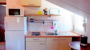 Cocina compacta equipada con microondas, lavamanos y una pequeña mesa con hervidor.