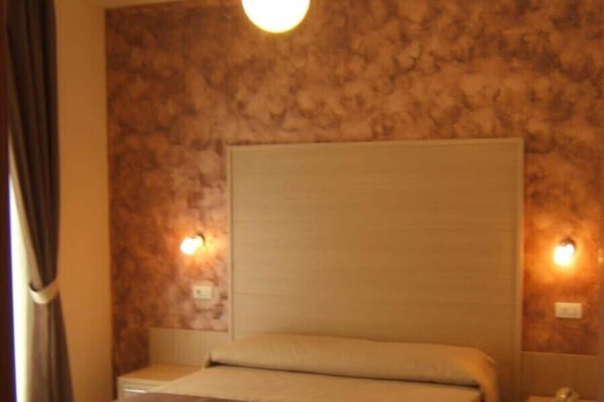 Ein Hotelzimmer mit einem großen Bett, einem Nachttisch, einer Lampe und einer Wandleuchte.