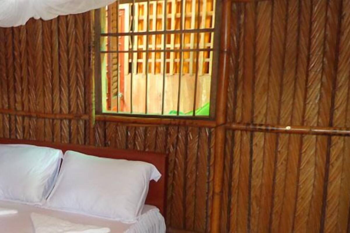 A room with a bed, a window with bars, and bamboo walls.