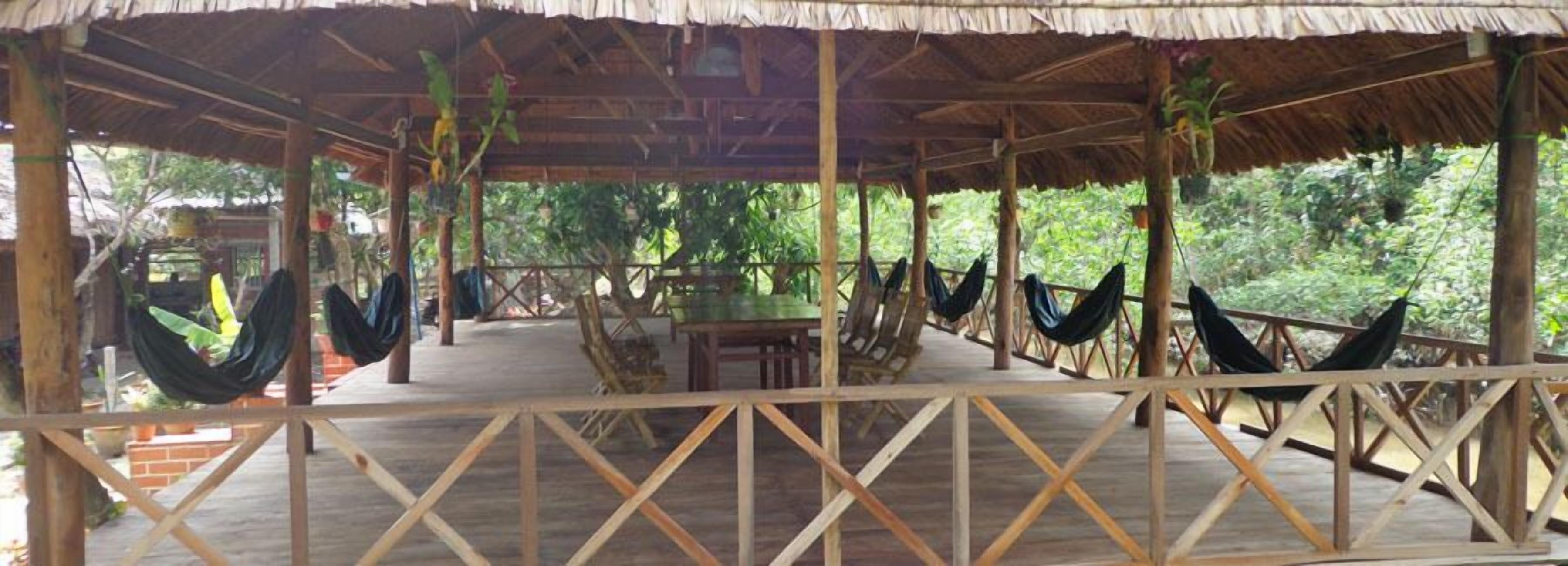A wooden deck with hammocks and a table, surrounded by lush greenery.