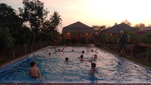A swimming pool surrounded by a grassy area with a few houses in the background. - Phuong Thao Homestay (An Binh)